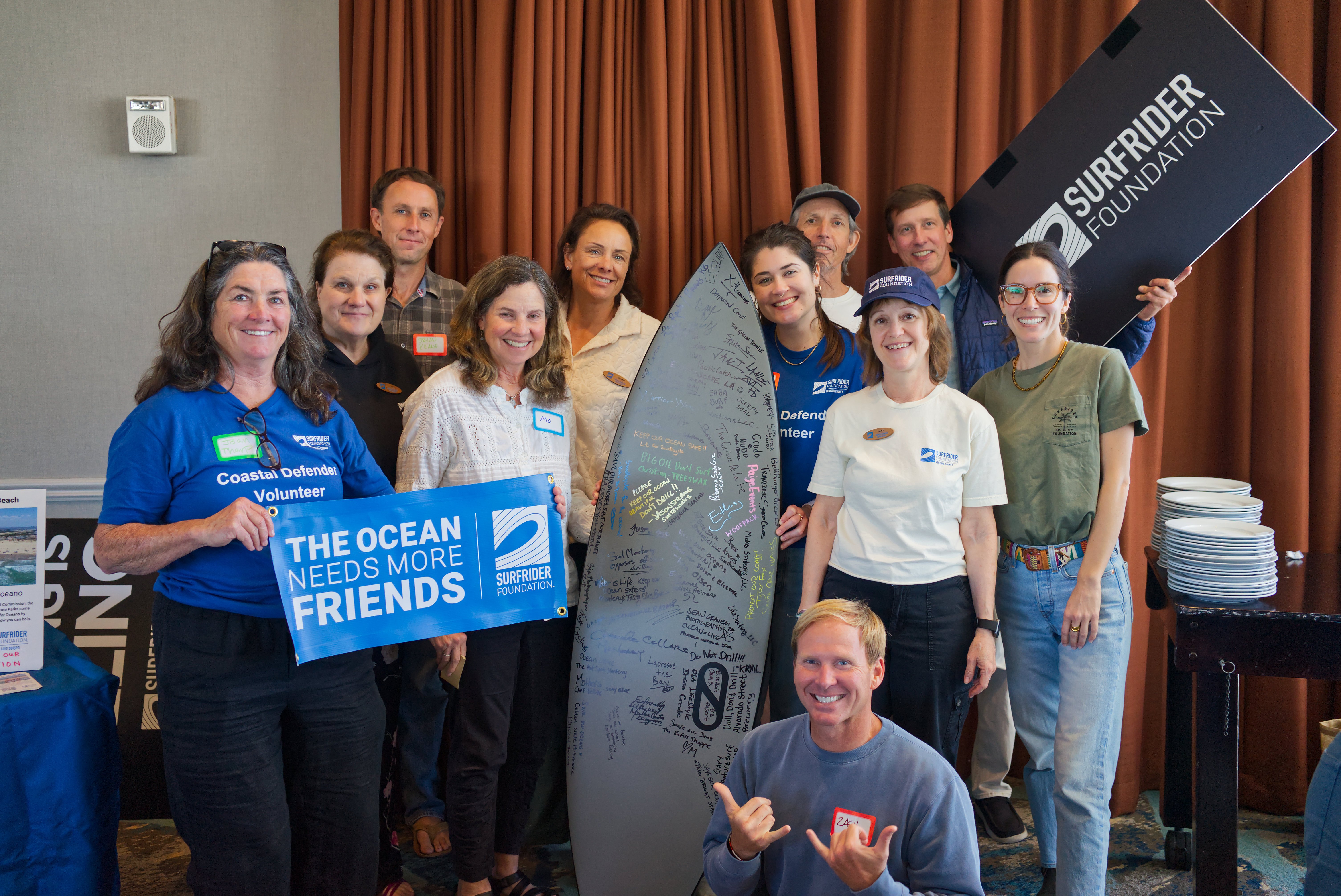 group posing with surfrider signs and surfboard