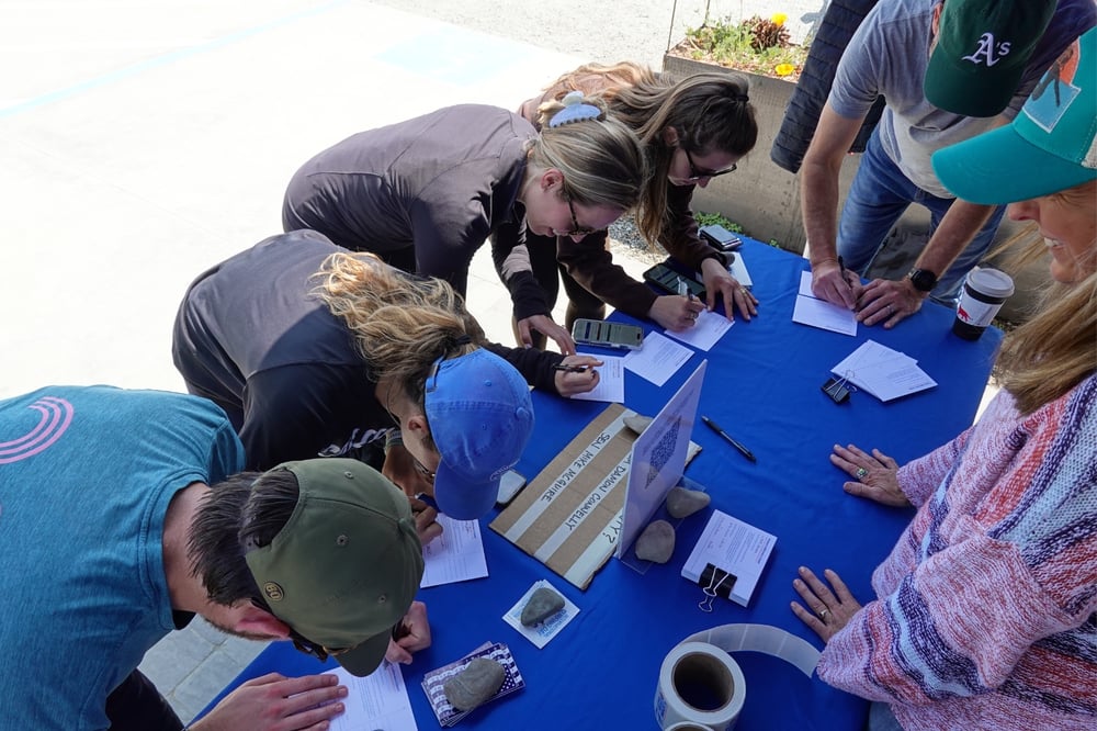 Five advocates sign postcards at a Surfrider table.