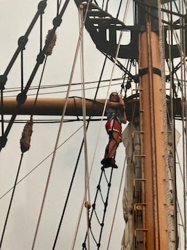 Woman in harness climbing high in the rigging of a sailboat