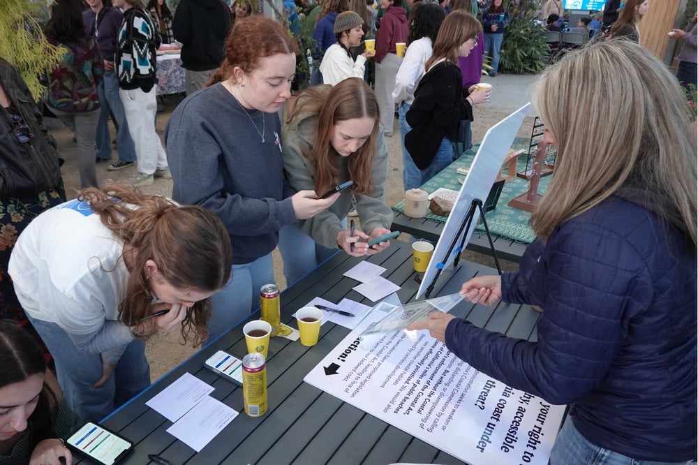 Three students sign postcards at a table.
