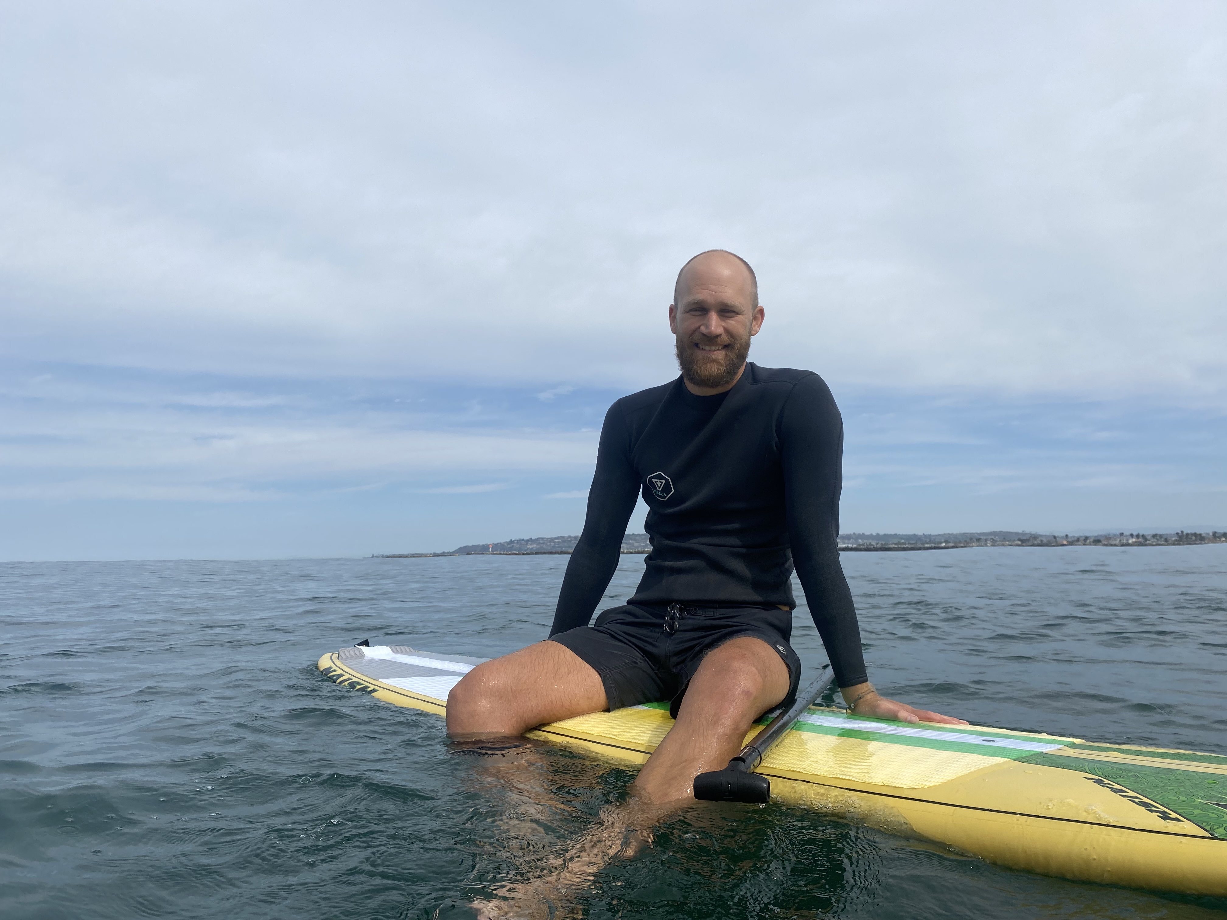 Mitch sits on a paddleboard out at sea, with a smile on his face.